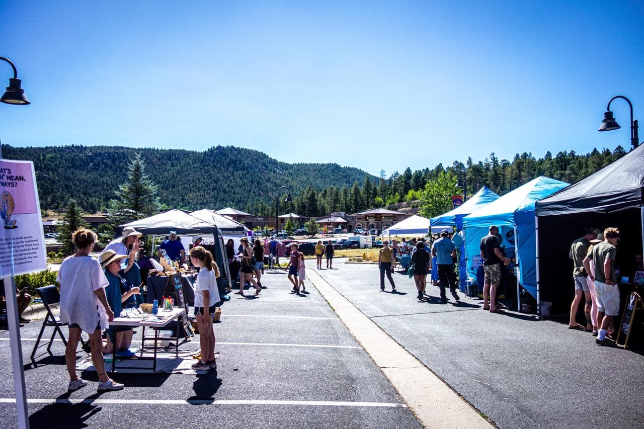 Vendor tents lining the lot at the Snowpack Cottage Market in Conifer, with the foothills behind
