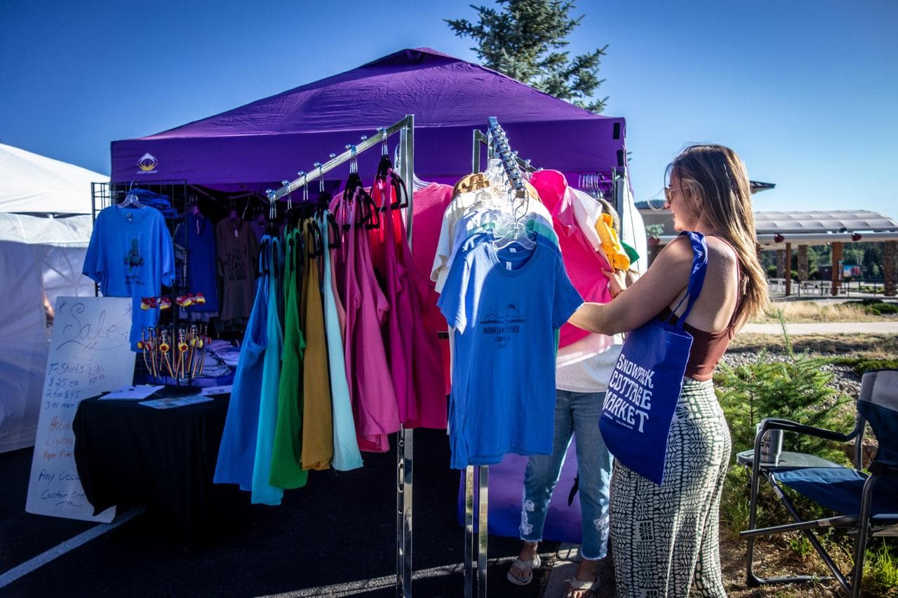 A shopper carrying a Snowpack Cottage Market tote browsing a rack of hand-printed shirts